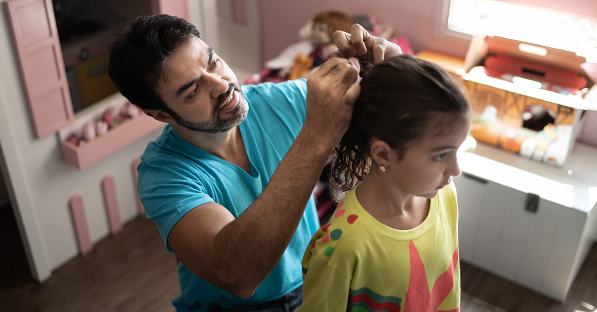 A single father putting his daughter's hair into a ponytail