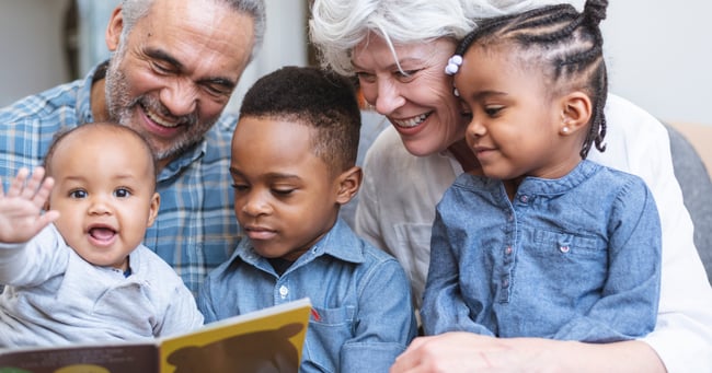 Three young children read a book with older adults